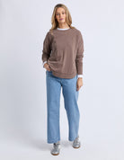 Woman wearing a brown sweater and blue jeans on a white background