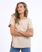 Woman wearing a beige t-shirt and blue pants against a white background