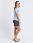 A woman modeling a light blue and white striped short-sleeve t-shirt, dark gray denim shorts, and beige platform sandals against a plain white studio background.