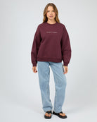 Person wearing a maroon sweatshirt with text and light blue jeans on a white background