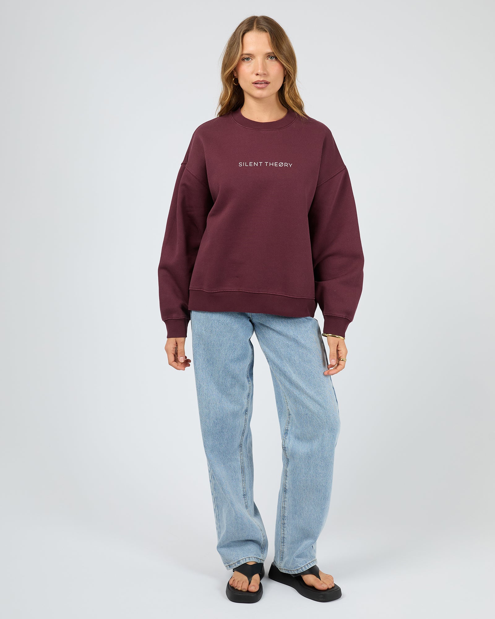 Person wearing a maroon sweatshirt with text and light blue jeans on a white background