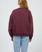 Person wearing a maroon sweatshirt and light blue jeans on a plain background