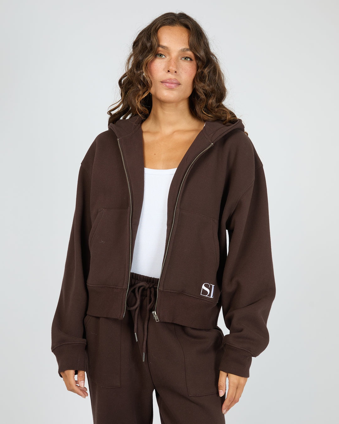 Woman wearing a brown tracksuit with a visible brand logo on a plain background