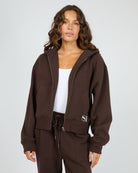 Woman wearing a brown tracksuit with a visible brand logo on a plain background