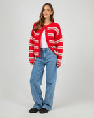 Woman wearing a red and white striped cardigan, white shirt, blue jeans, and black shoes on a white background