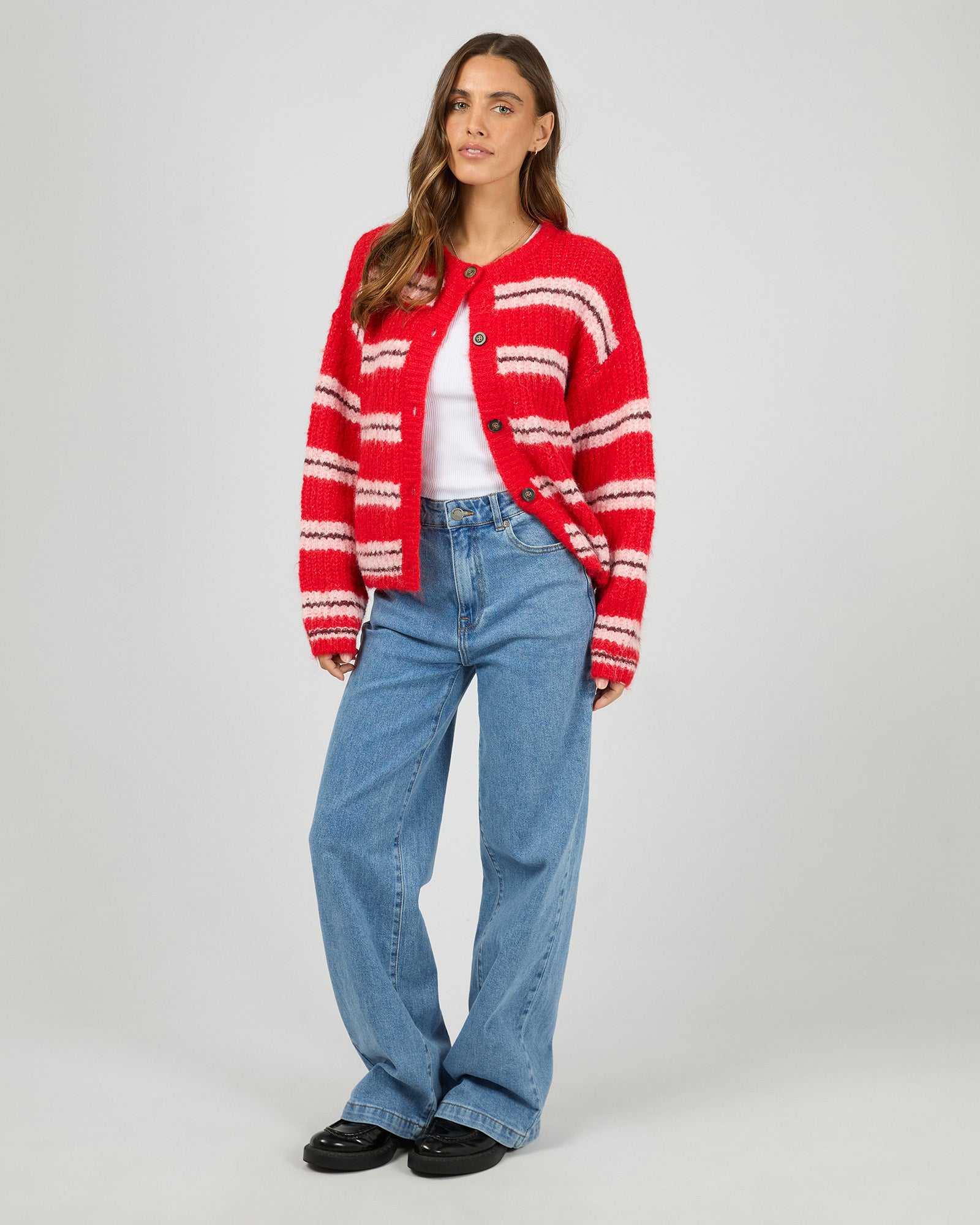 Woman wearing a red and white striped cardigan, white shirt, blue jeans, and black shoes on a white background