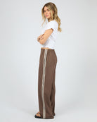 Woman wearing a white top and brown pants with a stripe on a white background