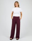 Woman wearing maroon pants with white stripes and a white shirt on a white background