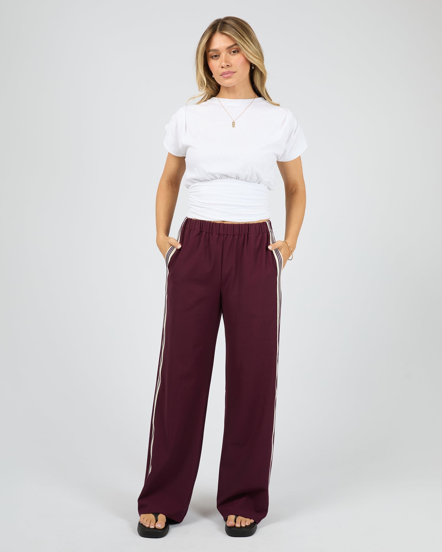 Woman wearing maroon pants with white stripes and a white shirt on a white background