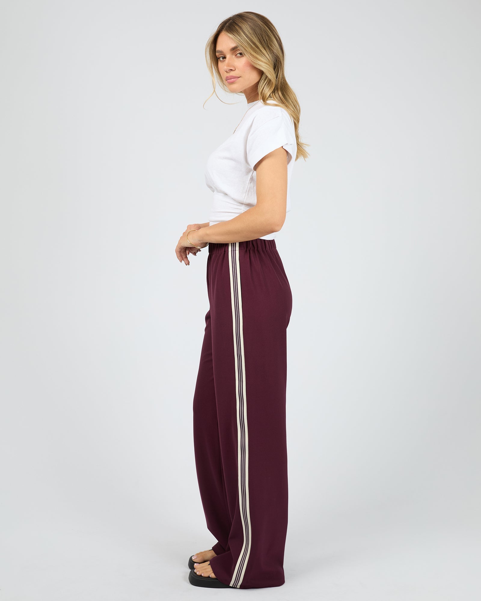 Woman wearing burgundy pants with a white stripe on a white background