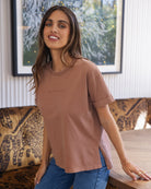 Woman wearing a brown t-shirt with text, standing in a room with a couch and painting.