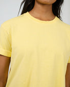 A close-up of a person wearing a pale yellow short-sleeve crewneck t-shirt with subtle tonal embroidery on the chest.