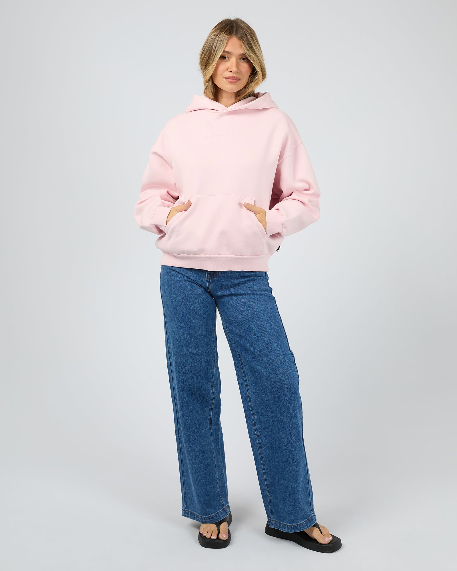 Woman wearing a pink hoodie and blue jeans on a white background