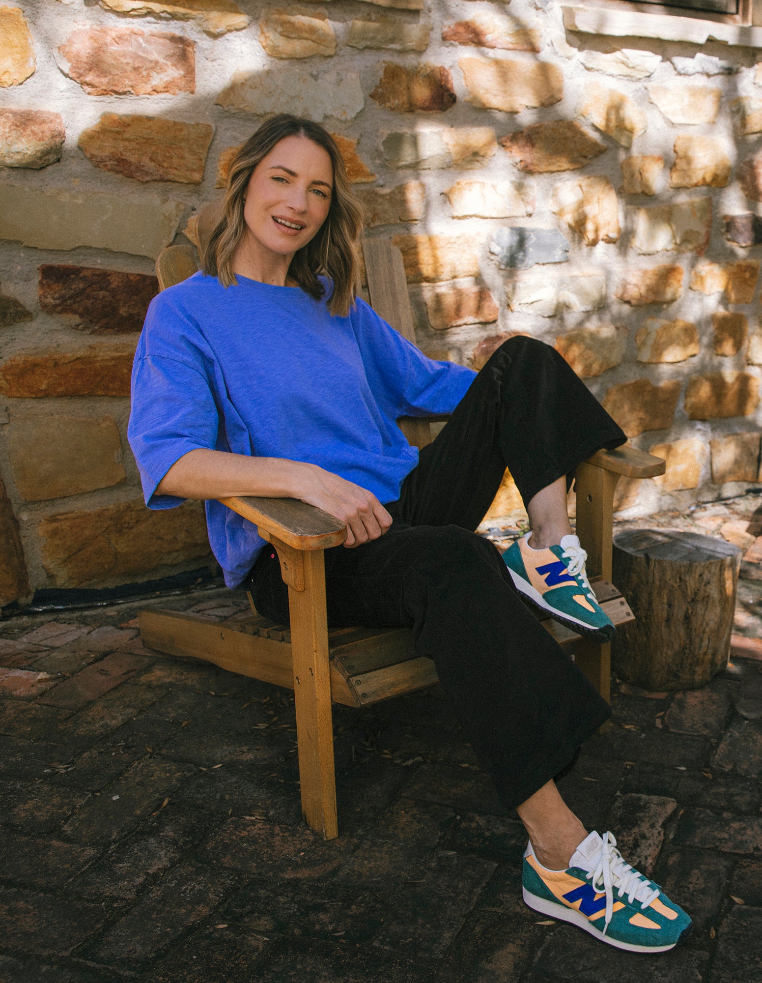 Woman sitting on a wooden chair against a stone wall