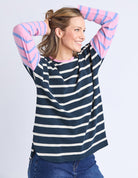 Woman wearing a navy and white striped sweater with pink sleeves on a light gray background