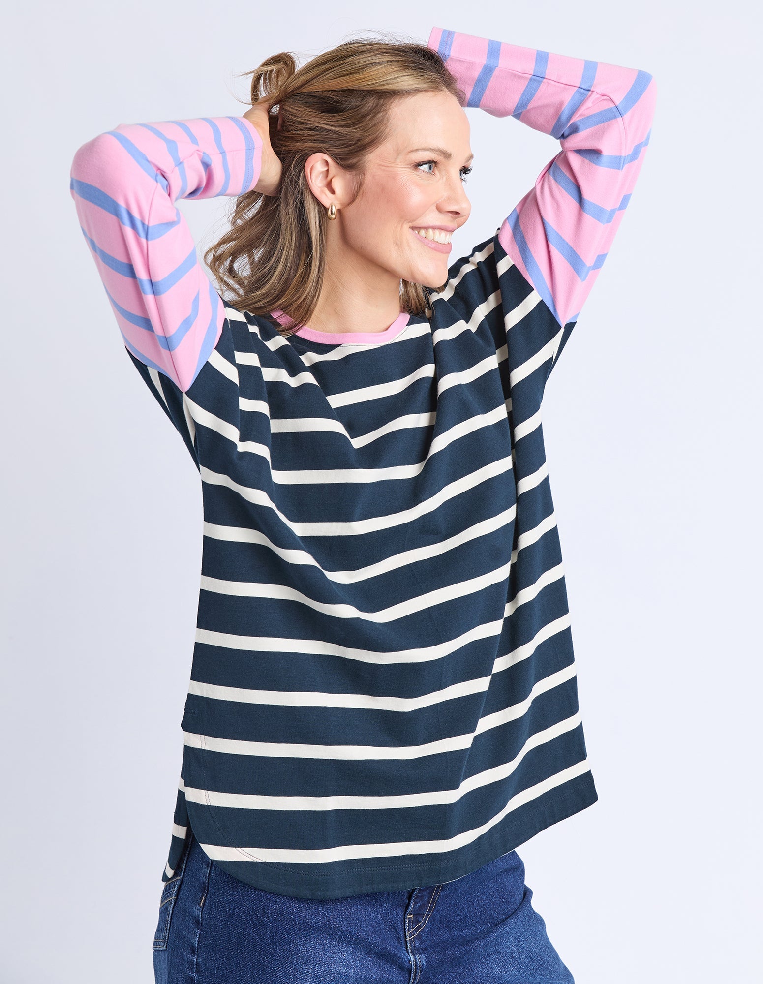 Woman wearing a navy and white striped sweater with pink sleeves on a light gray background