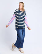 Woman wearing a striped long-sleeve top and jeans on a light purple background