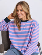 Woman wearing a pink and blue striped sweater sitting on a chair.