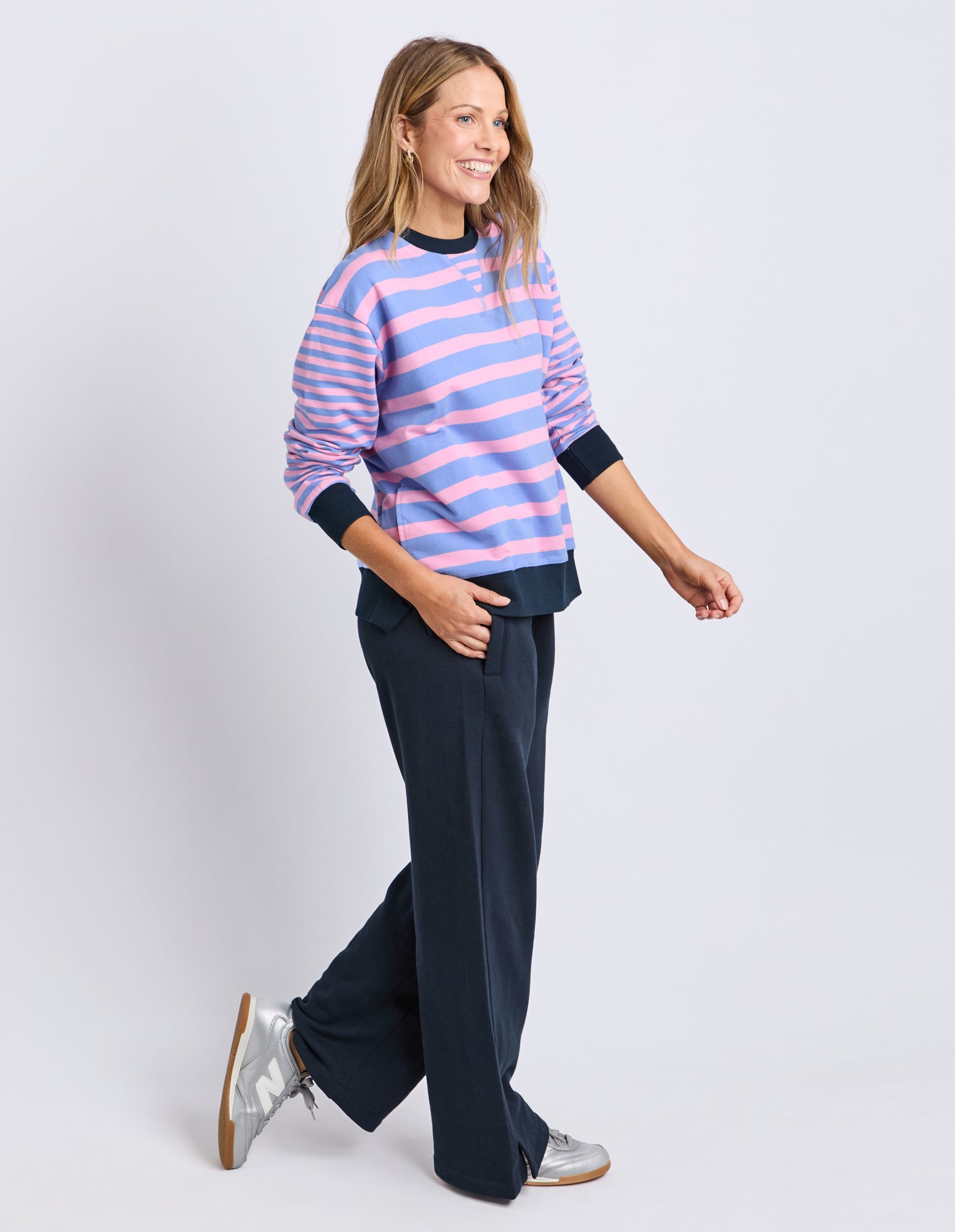 Woman wearing a striped sweater and dark pants on a light gray background