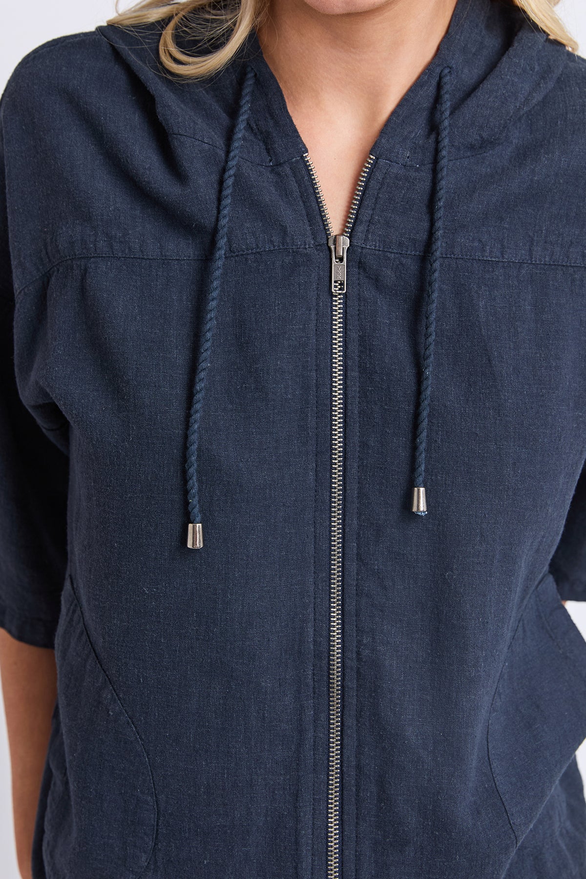 A close-up of a person wearing a navy blue zip-up hooded top with drawstrings and a textured fabric.