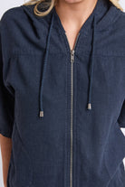 A close-up of a person wearing a navy blue zip-up hooded top with drawstrings and a textured fabric.