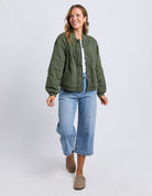 Woman wearing a green quilted jacket and blue jeans on a white background