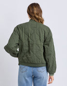 Person wearing a green quilted jacket and blue jeans on a white background