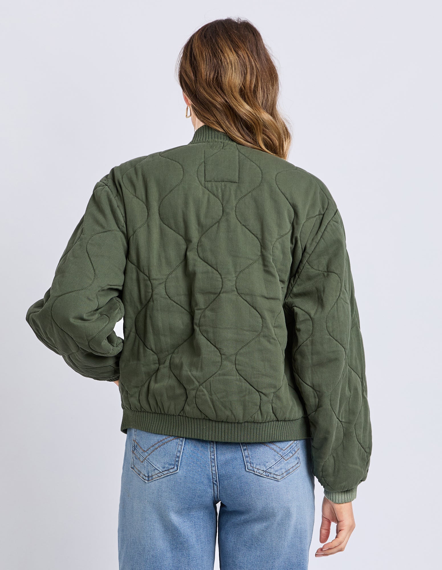 Person wearing a green quilted jacket and blue jeans on a white background
