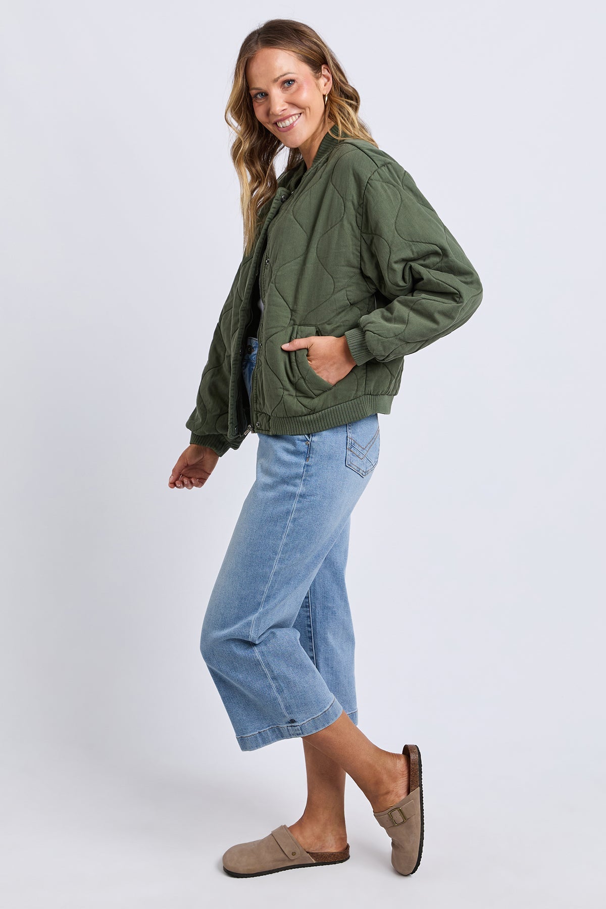 Woman wearing a green jacket and light blue jeans on a white background
