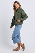 Woman wearing a green jacket and light blue jeans on a white background