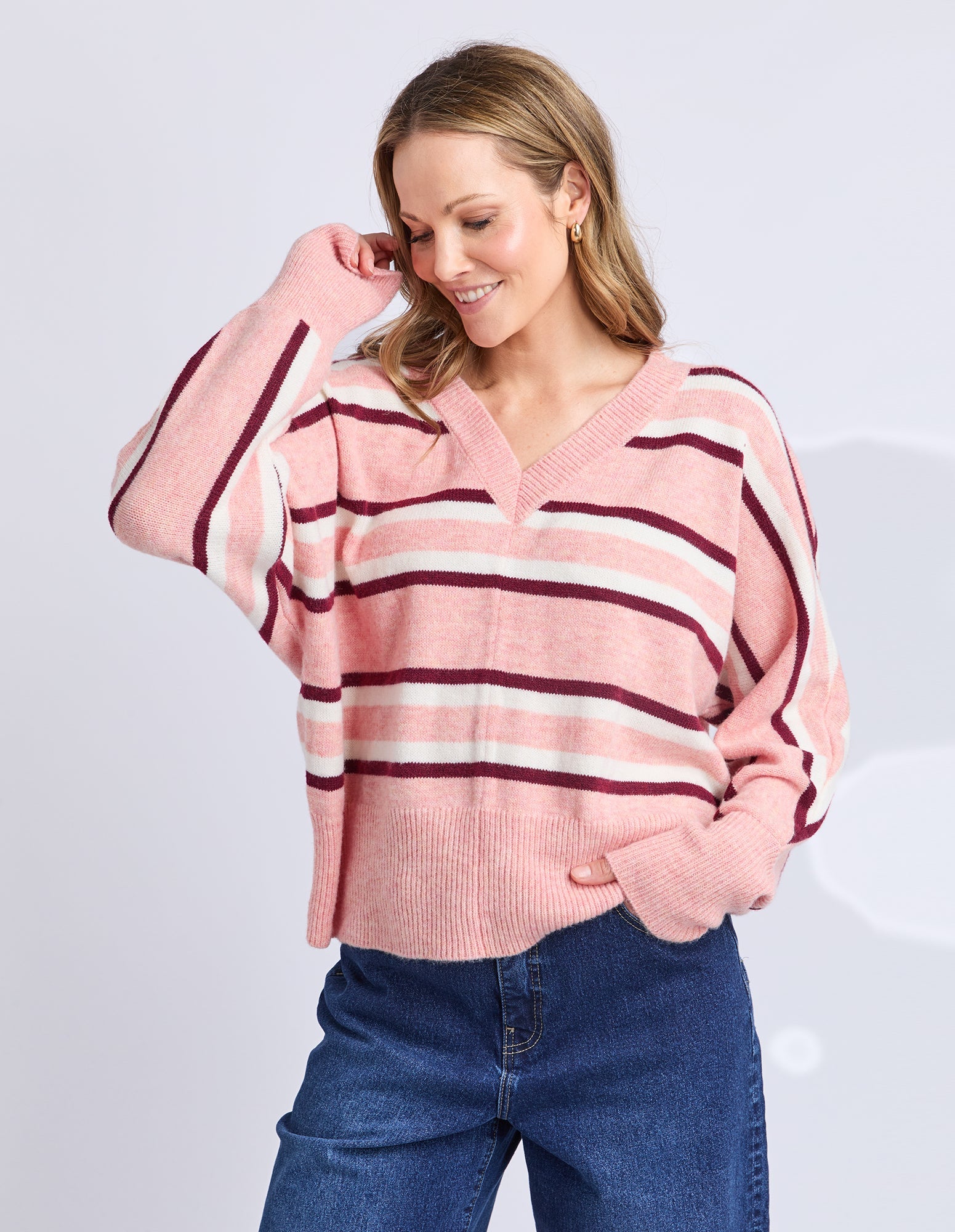 Woman wearing a pink and red striped sweater with blue jeans on a light gray background