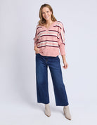 Woman wearing a pink striped sweater and blue jeans on a white background