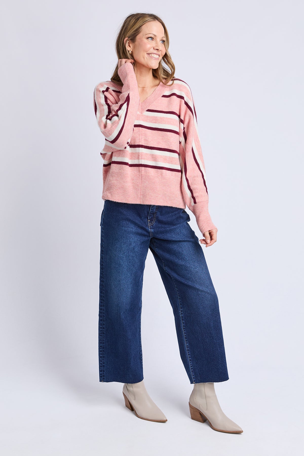 Woman wearing a pink striped sweater and blue jeans on a white background