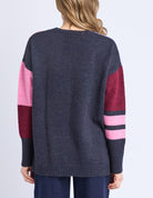 Person wearing a dark gray sweater with pink and red sleeves on a light purple background