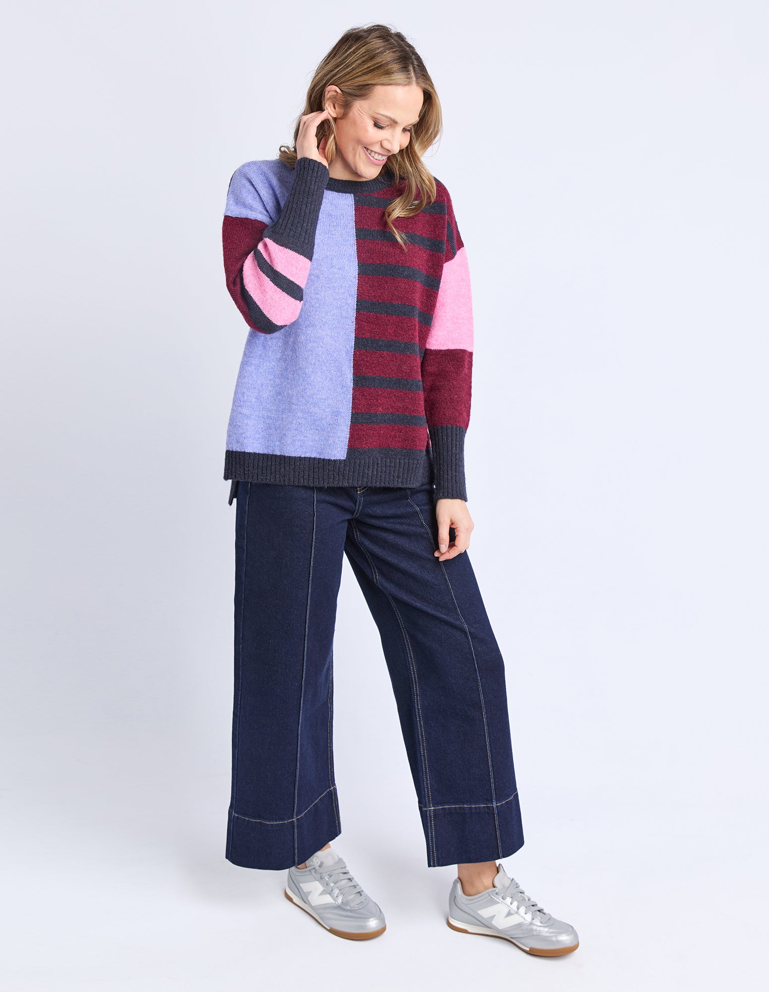 Woman wearing a colorful sweater and dark jeans on a white background