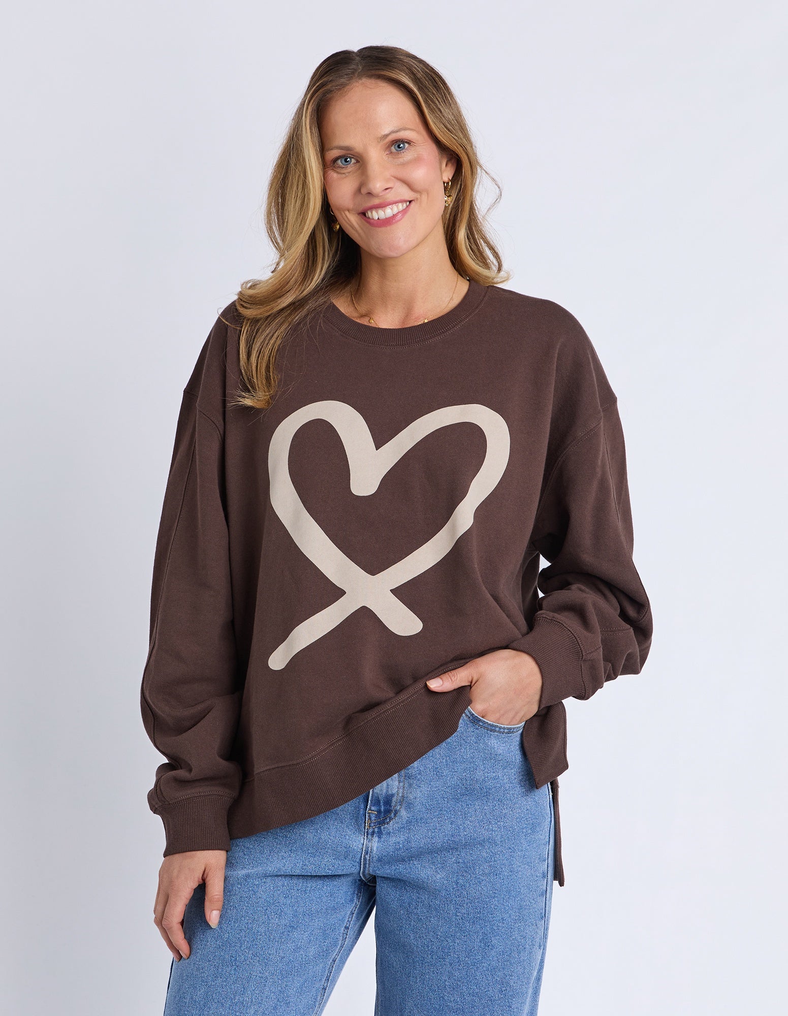 Woman wearing a brown sweatshirt with a heart design on a plain background