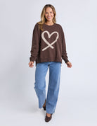 Woman wearing a brown sweatshirt with a heart design and blue jeans on a white background