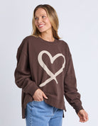 Woman wearing a brown sweatshirt with a heart design on a light gray background
