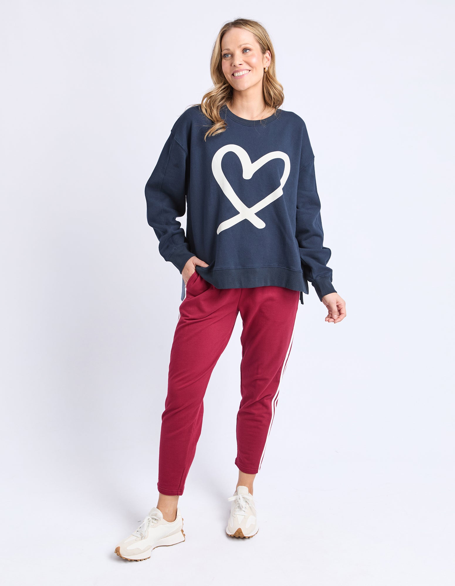 Woman wearing a navy sweatshirt with a heart design and red pants on a white background
