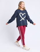 Woman wearing a navy sweatshirt with a heart design and red pants with white stripes on a light gray background