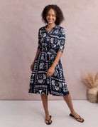 Woman wearing a navy blue dress with white patterns against a beige background