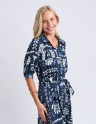 Woman wearing a navy dress with white floral pattern on a light gray background