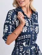 Woman wearing a navy blue dress with white geometric pattern on a plain background