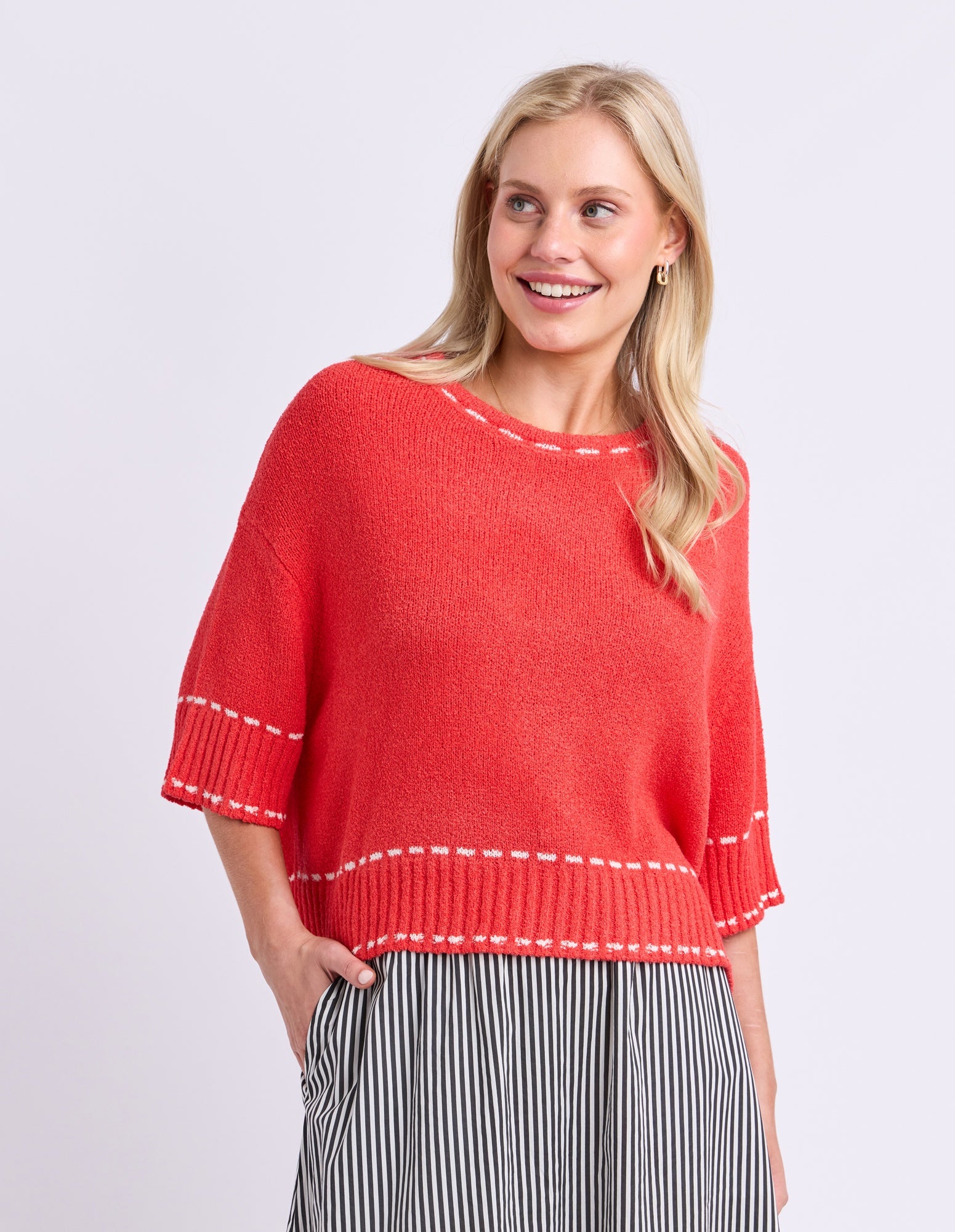 Woman wearing a red sweater with white trim on a plain background