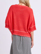Red sweater with white trim worn by a person on a light purple background