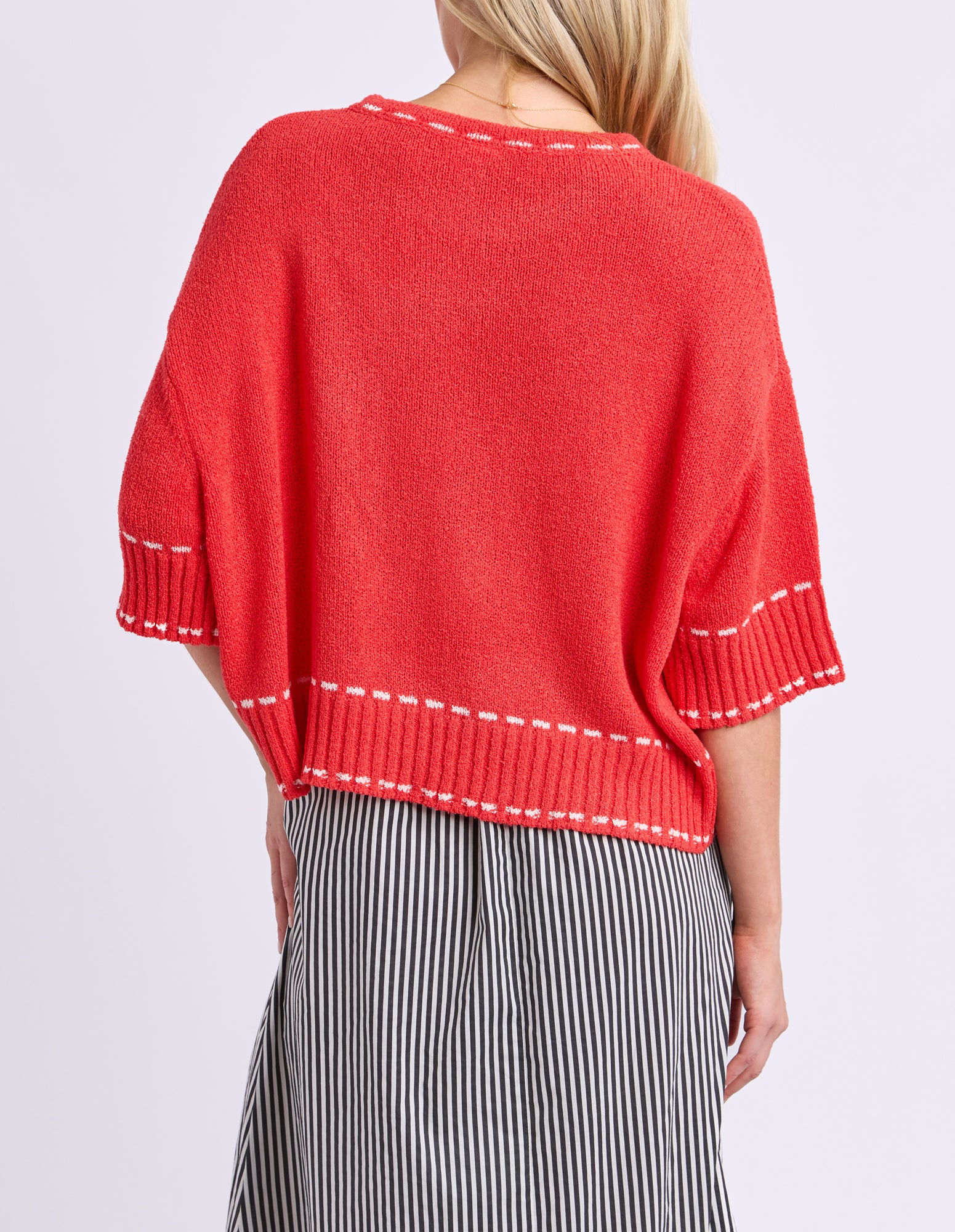 Red sweater with white trim worn by a person on a light purple background