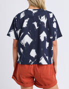 Person wearing a navy blue and white abstract patterned top with orange shorts on a white background