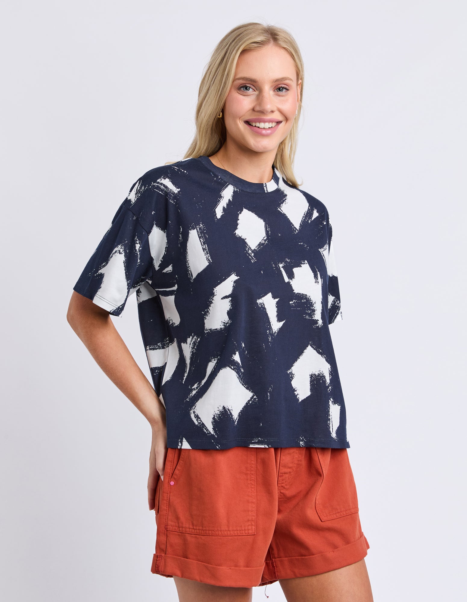 Woman wearing a navy blue t-shirt with white abstract patterns and orange shorts on a light gray background