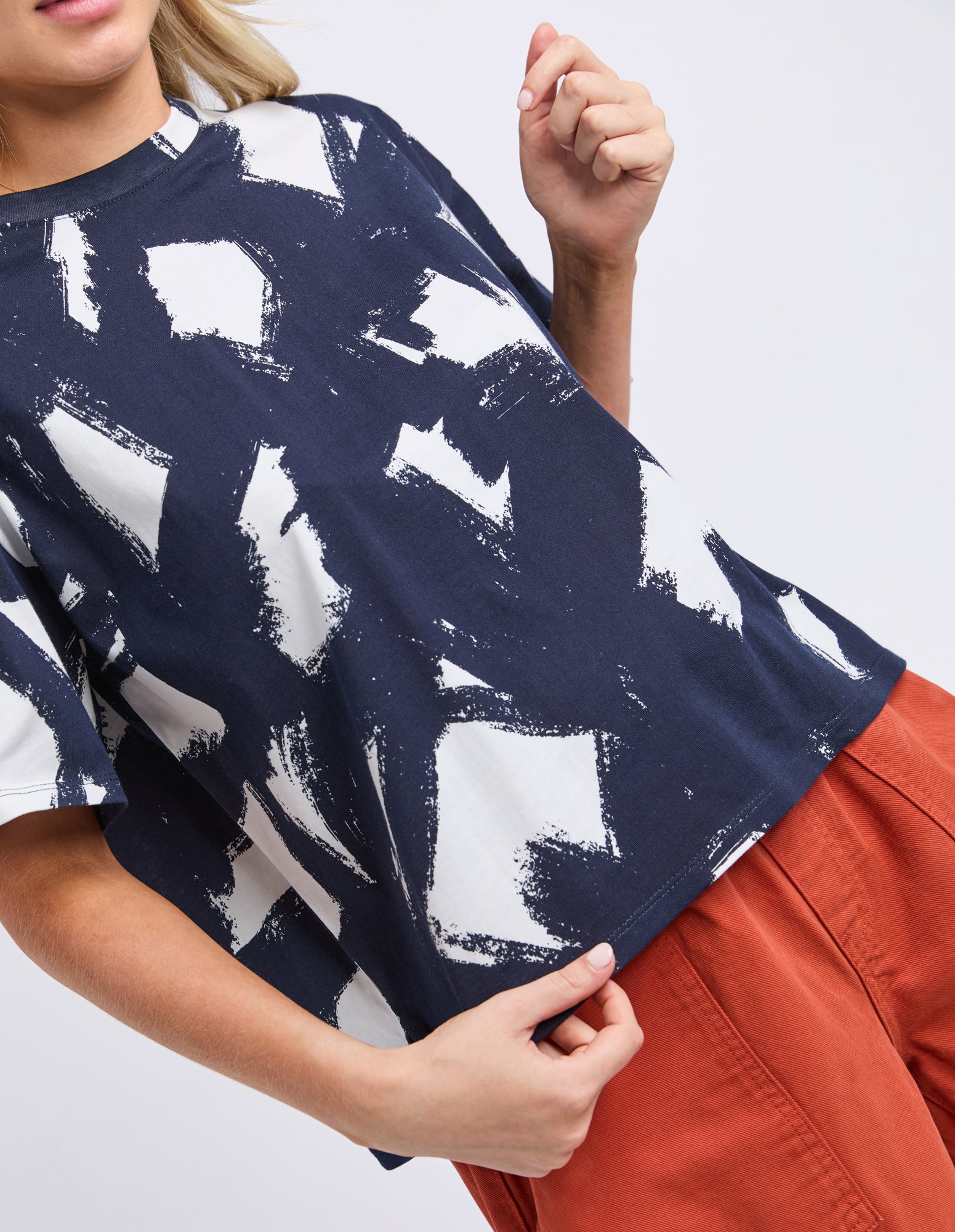Person wearing a navy blue t-shirt with white abstract patterns and orange pants on a light gray background