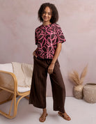 Woman wearing a pink and black patterned top with brown pants in a minimalistic setting.